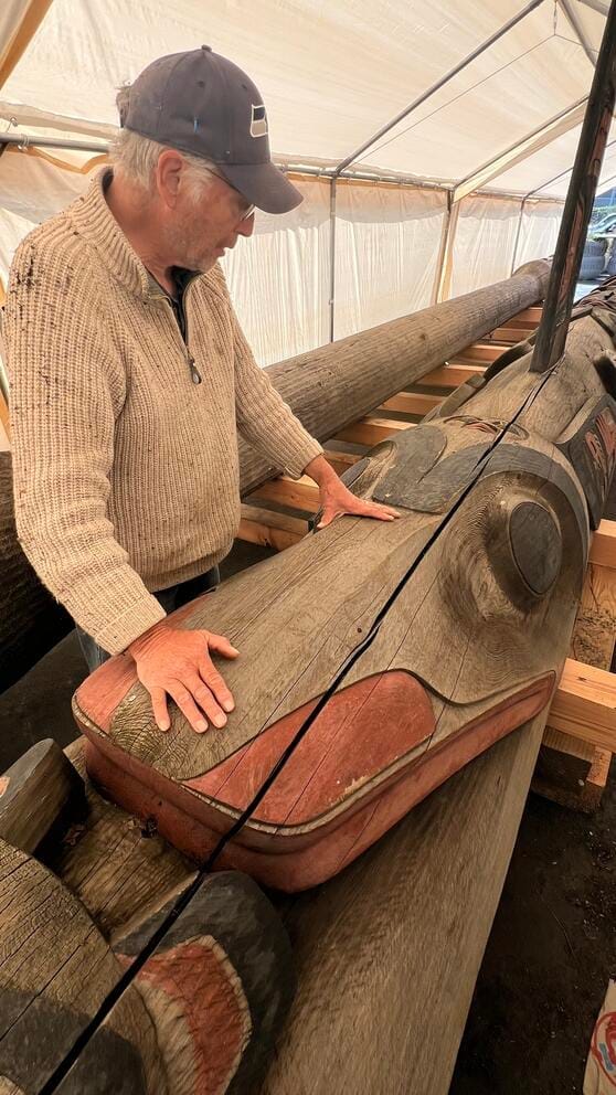 A person inspects a crack on a totem pole.