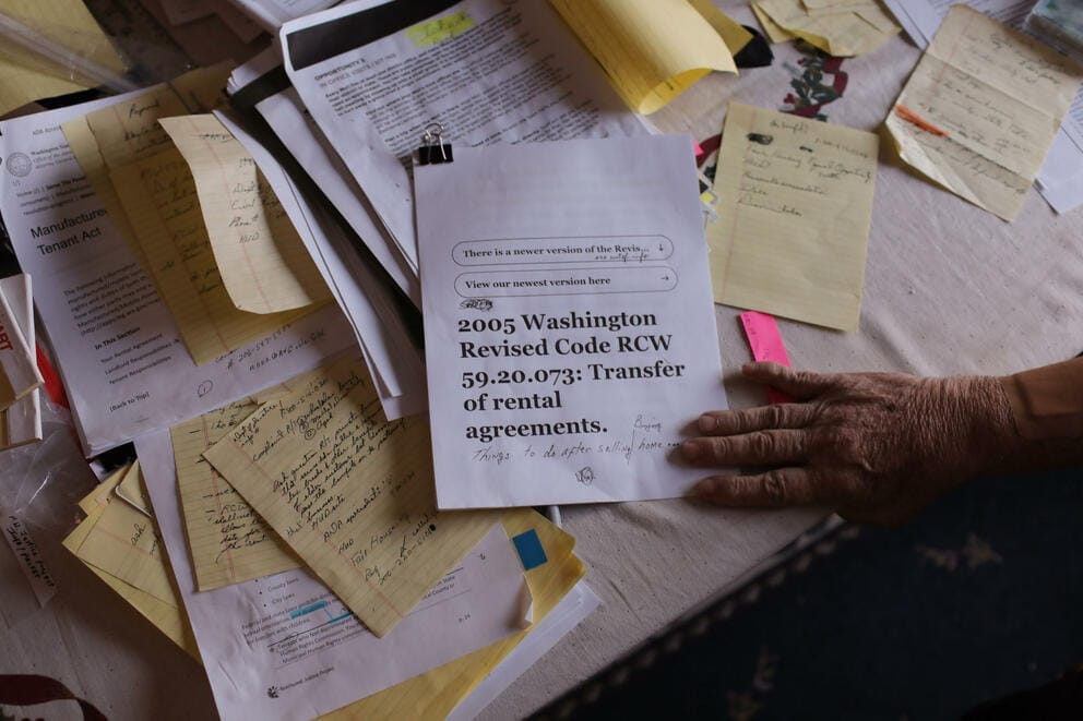 Scattered paperwork covers a desk with a hand reaching into the frame
