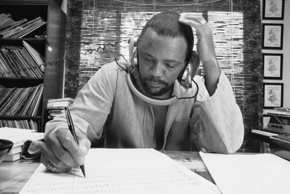 black and white 1970s photo of Quincy Jones writing in a music studio with headphones on