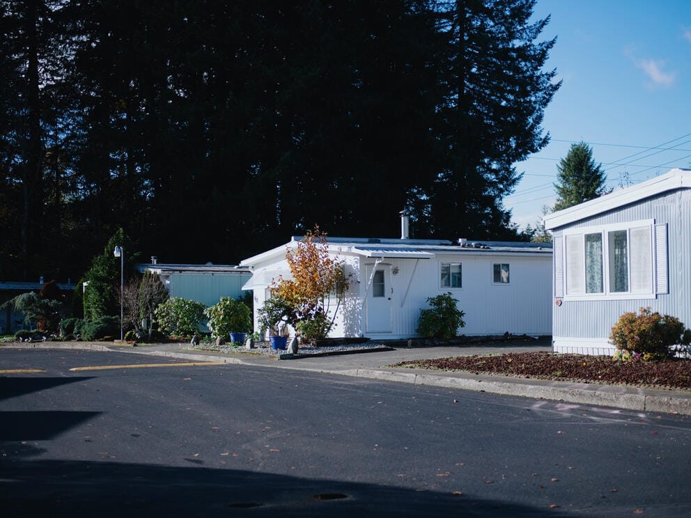 Three mobile home sit along a sunlit street with trees in the background