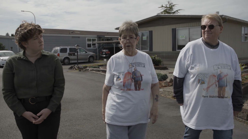 Journalist Jaelynn Grisso walks down the street of a mobile home park with residents Caroline Hardy and Deb Wilson