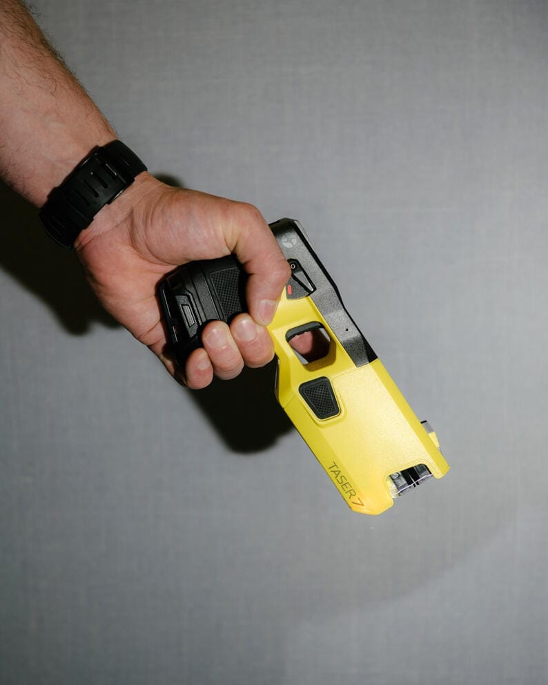 a hand aims a yellow taser