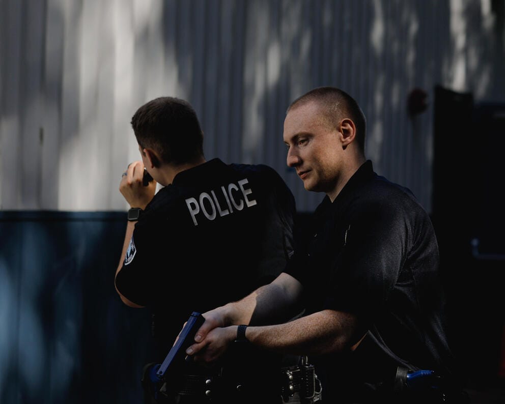 Two police recruits do a training exercise while holding training guns and flashlights behind a building