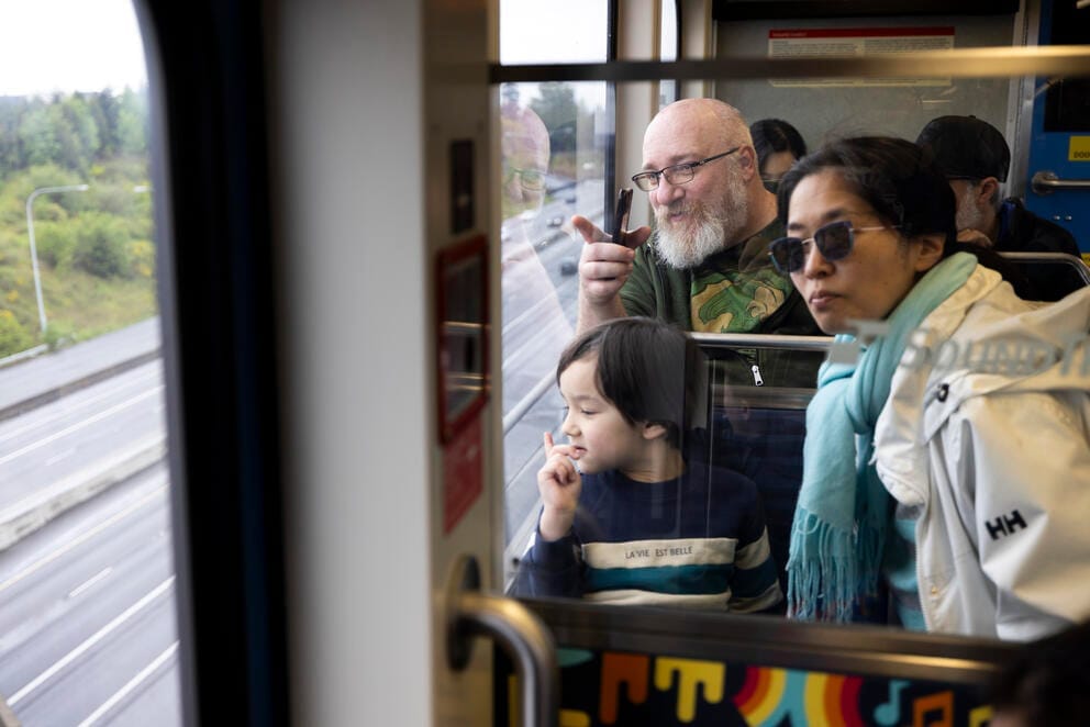 A man, a woman and a small child look out the window of a moving light rail car