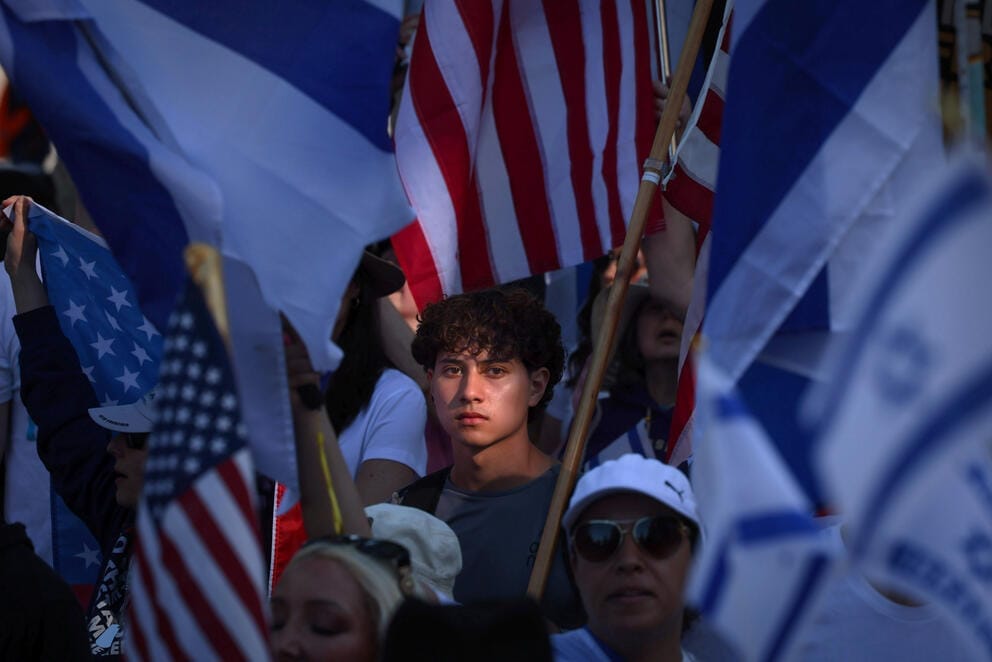 American and Israeli flags surround the face of a young man in a crowd illuminated by sunlight