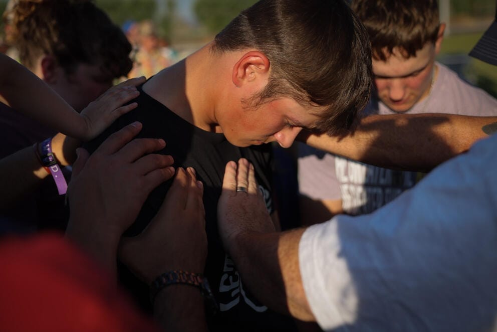 many hands reach out to touch a young man with his head bowed