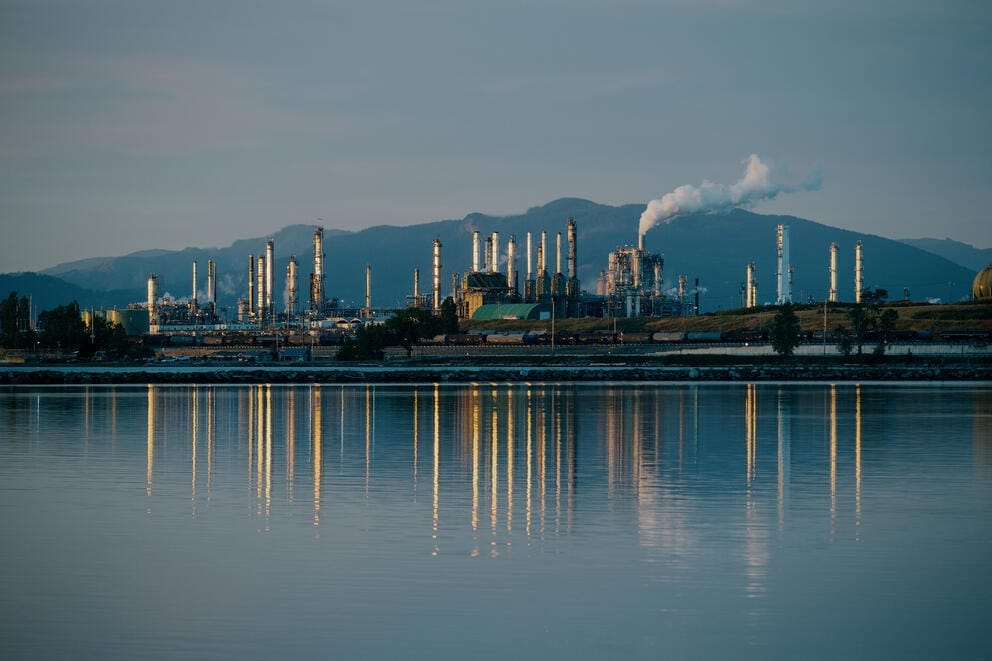 An oil refinery is reflected from across the water at dusk