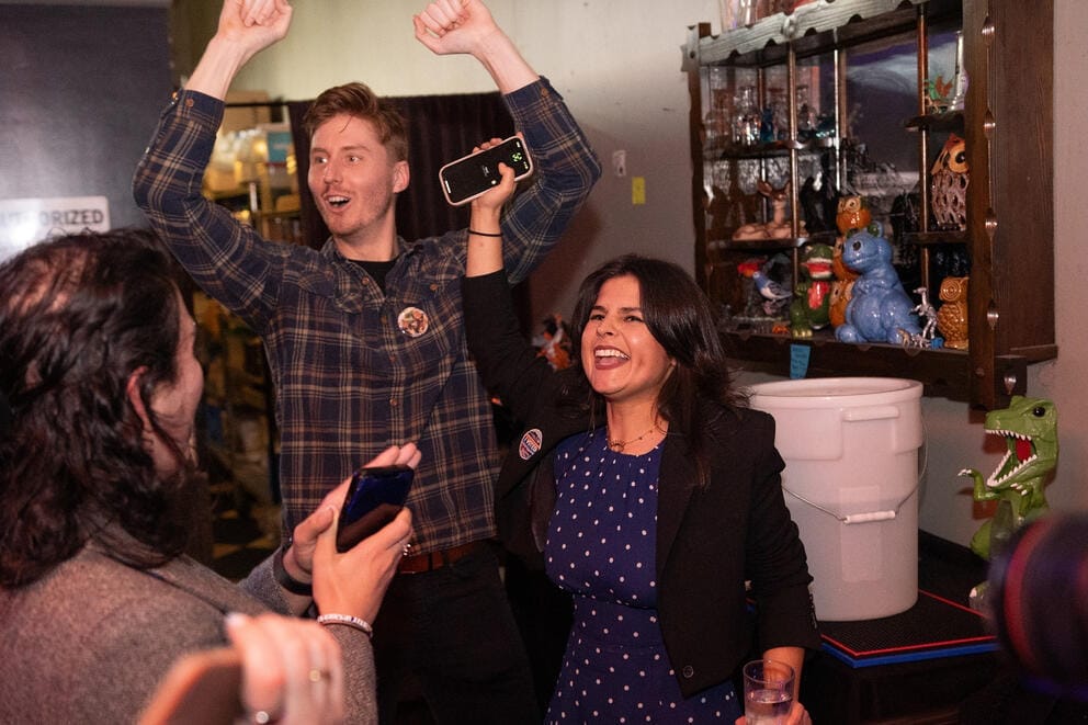 A man and a woman excitedly cheer with their hands up in the air