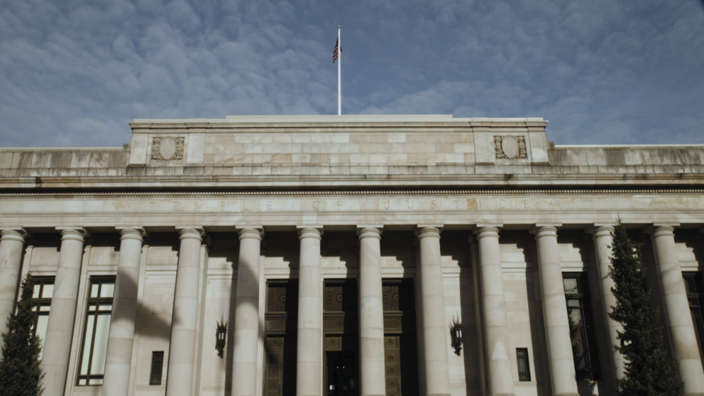 the outside of the temple of justice, a light-colored stone building with columns in the front