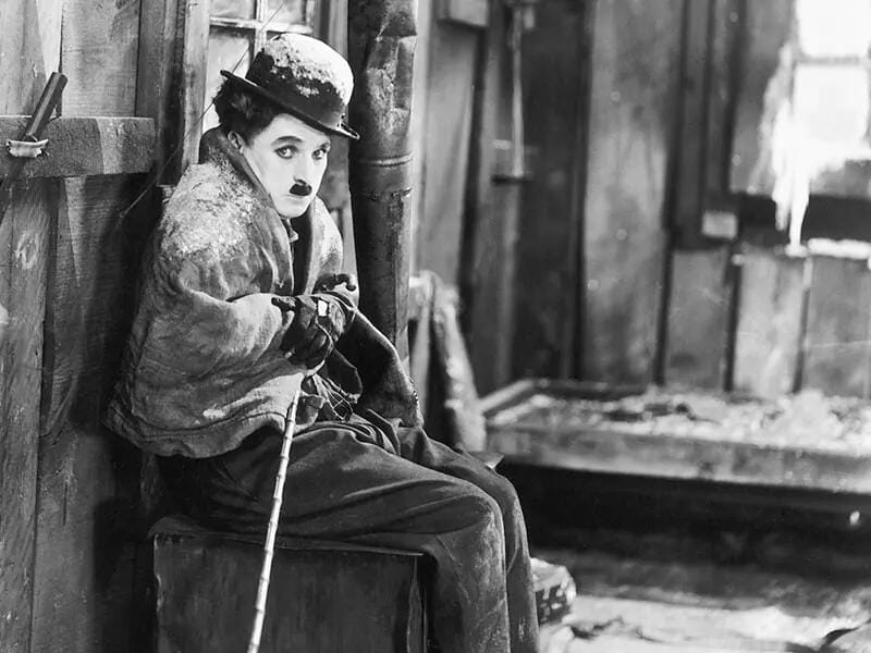 black and white still photo of Charlie Chaplin on a snowy movie set