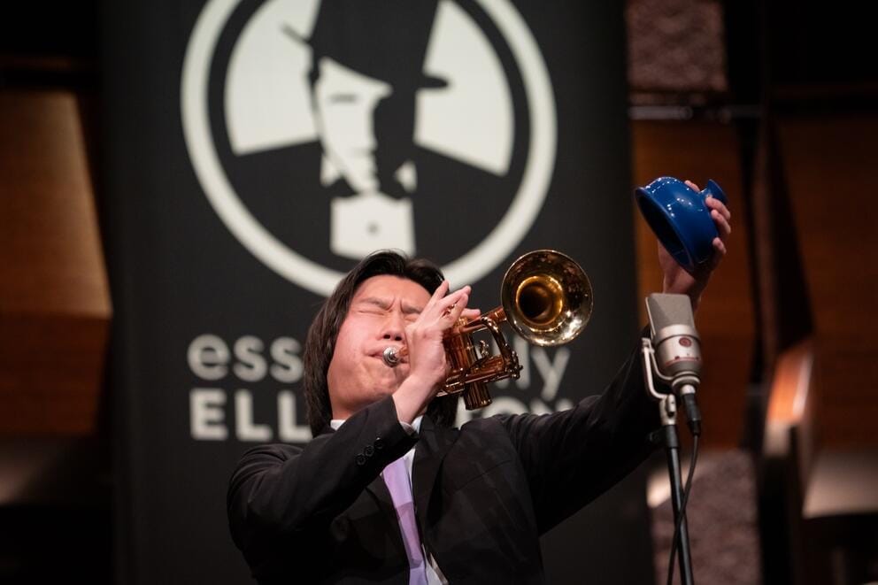photo of a young person playing the trumpet in front of a sign reading Essentially Ellington