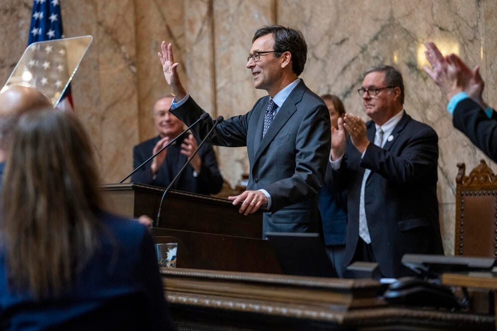 Bob Ferguson speaks at a podium as politicians stand and clap behind him