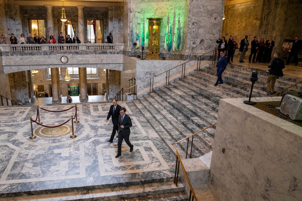 Bob Ferguson and another man walk down the stairway near the state seal of Washington in the capitol rotunda
