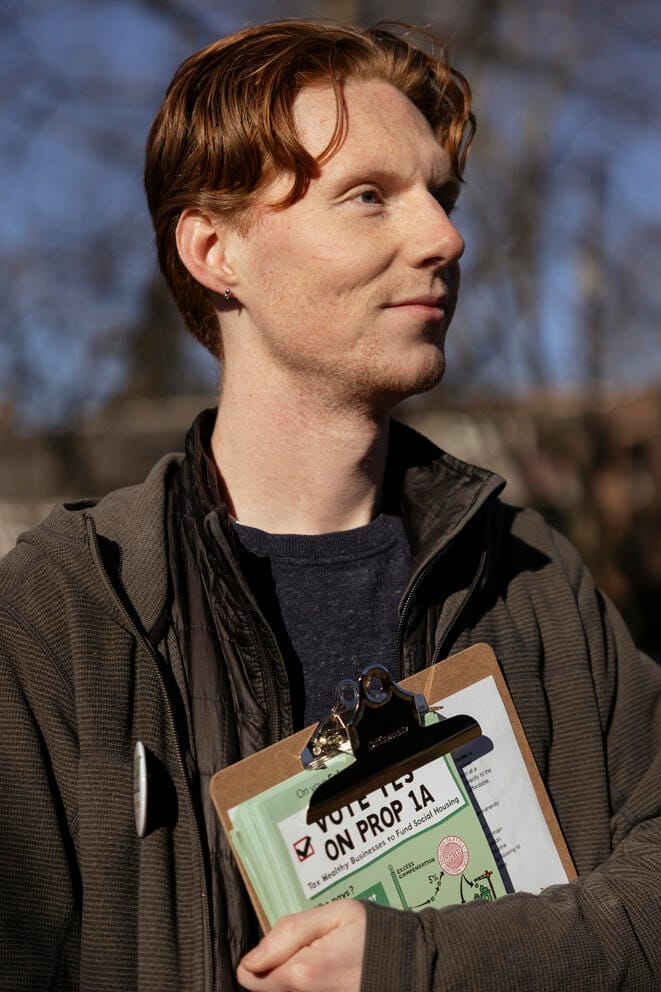 a man with red hair stands holding a clipboard with campaign materials