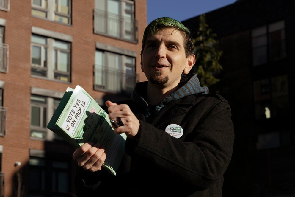a person with green hair and a black jacket stands holding a clipboard