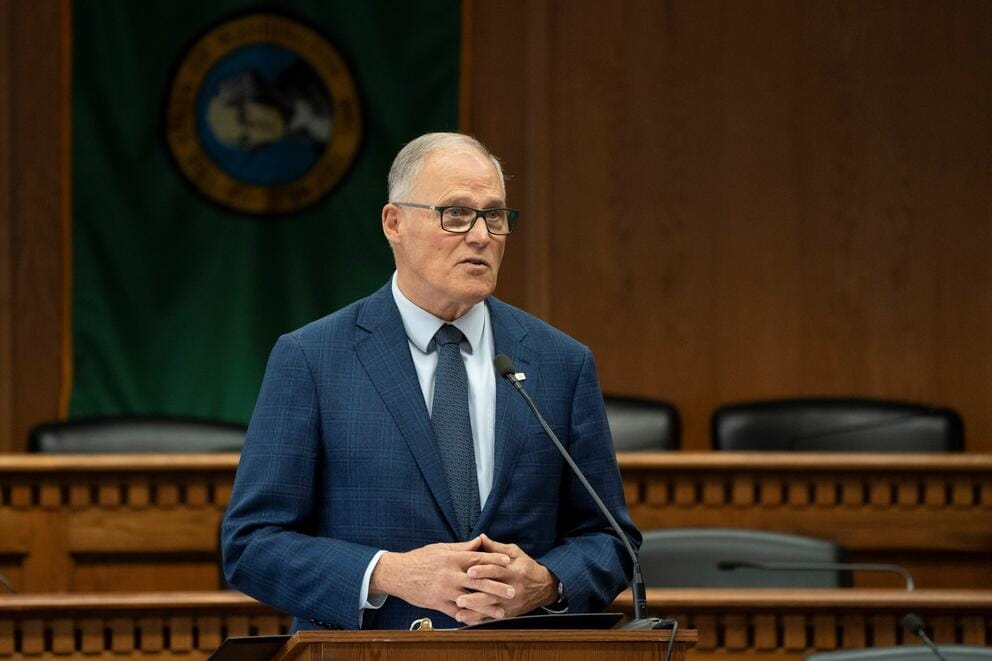 Former Gov. Jay Inslee gives a speech with an empty chamber behind him