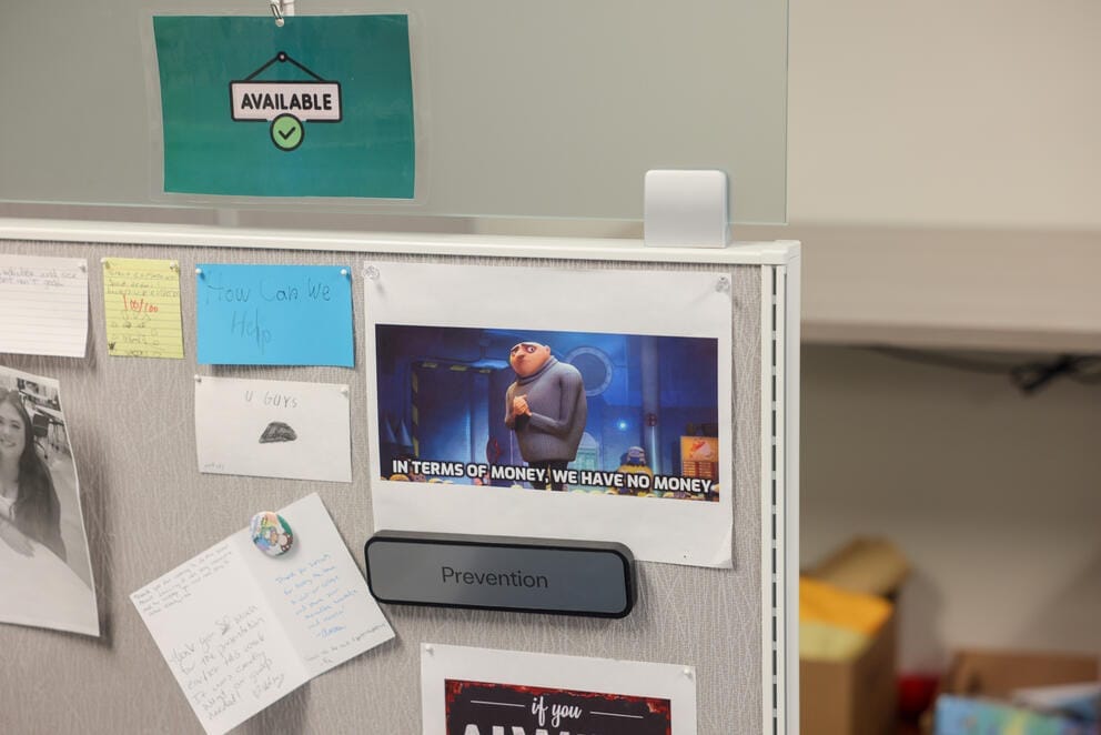 cards and photographs pinned to the side of a gray cubicle wall