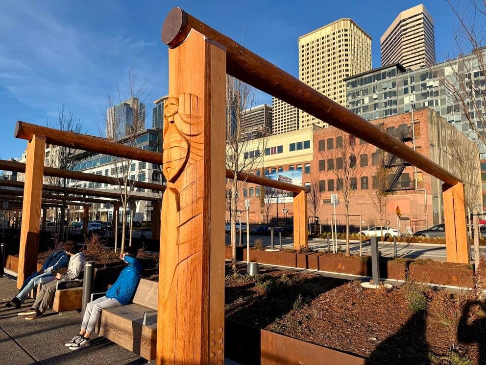 photo of an open post-and-beam structure in a downtown setting, with a carving on one pole