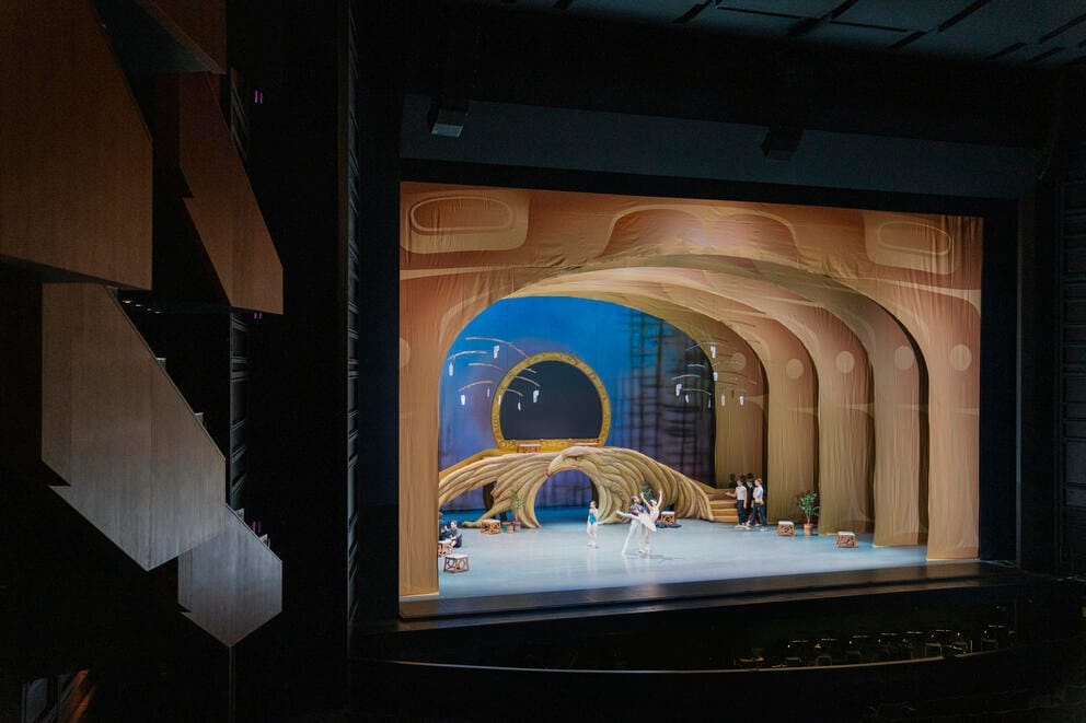 photo of an auditorium and stage set with arched wings, with dancers rehearsing