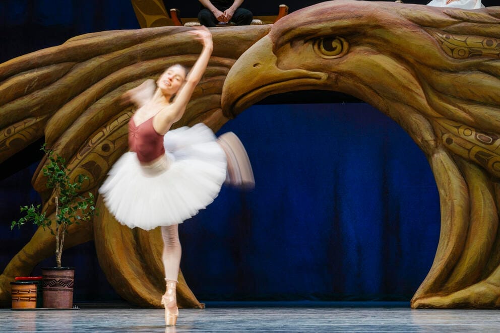 a ballet dancer in a tutu rehearses on a stage with a large eagle set piece