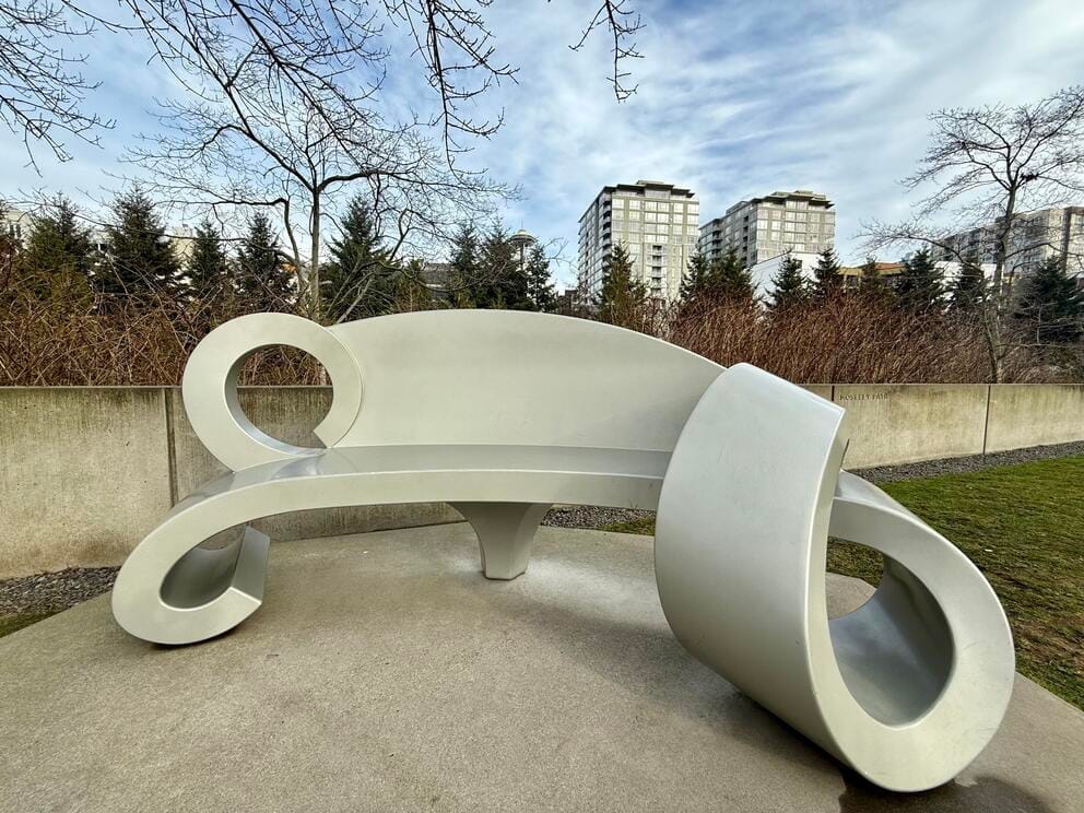 photo of a sculpture of a curly silver bench in a park