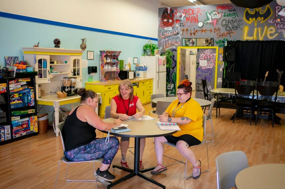 Two youth center staffers sit with a client at a round table in a brightly colored room