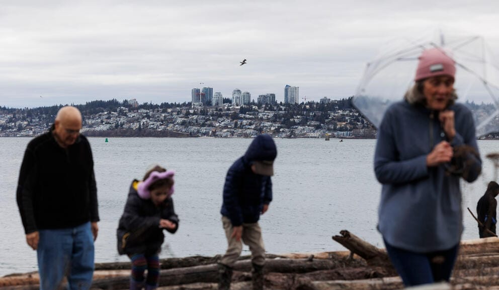 Four people walk away from water, and a skyline is seen in the background.