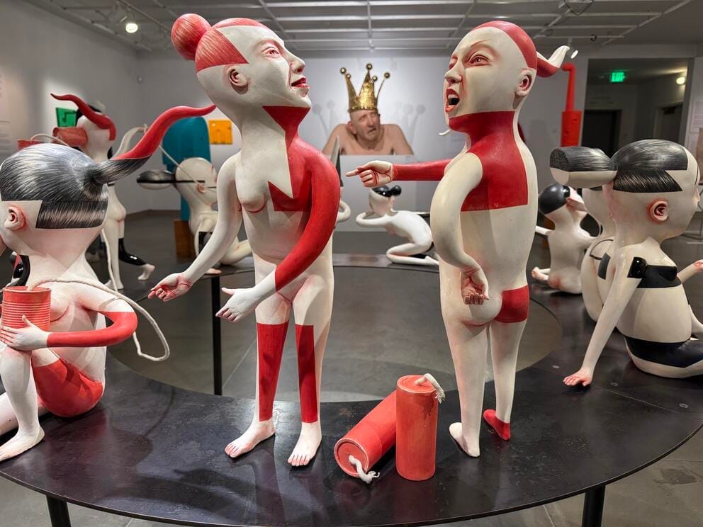 photo of a sculpture featuring several white and red figures arguing with each other