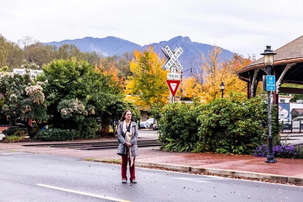 A person stands in the middle of a small town road, with a railroad crossing behind.