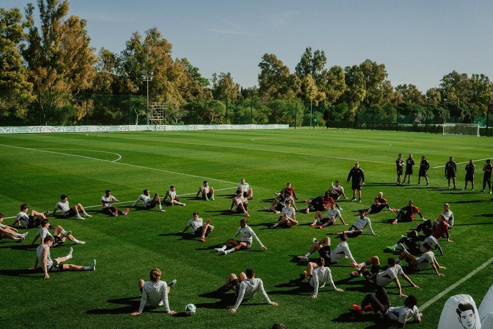 The Sounders team sit on a soccer field and stretch