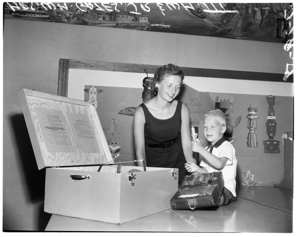 A woman and a child in front of an open chest in a black and white photo.
