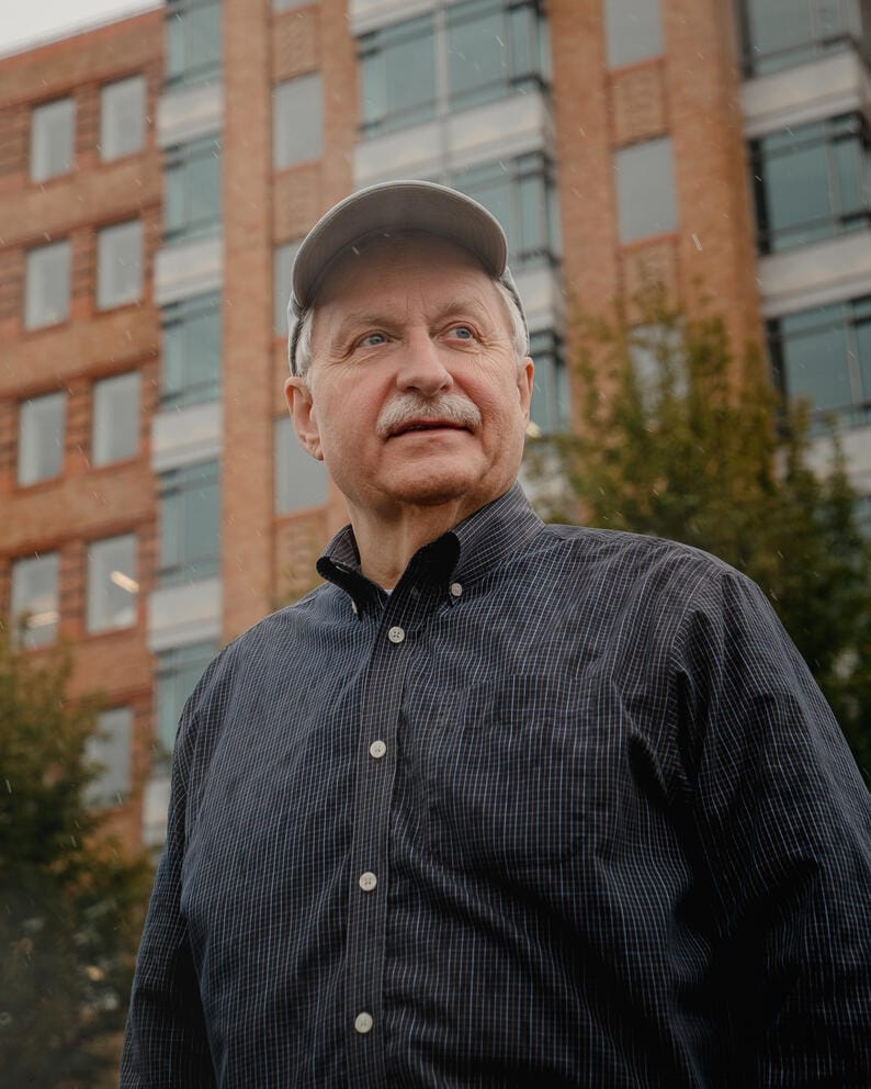a white man with a gray mustache weather a blue shirt and a cap
