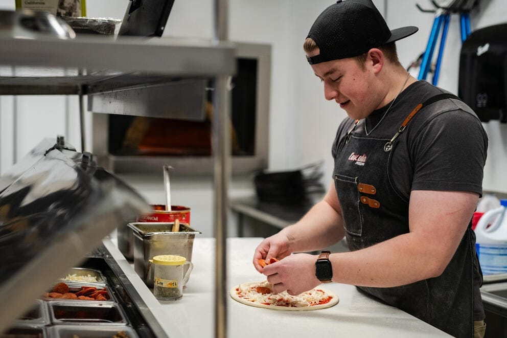 A worker at Cascadia Pizza sprinkles pepperoni onto a pizza