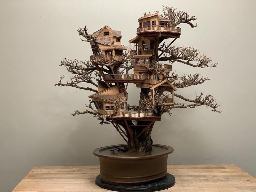 a bonsai tree on a pedestal to which has been added several tiny wooden treehouses