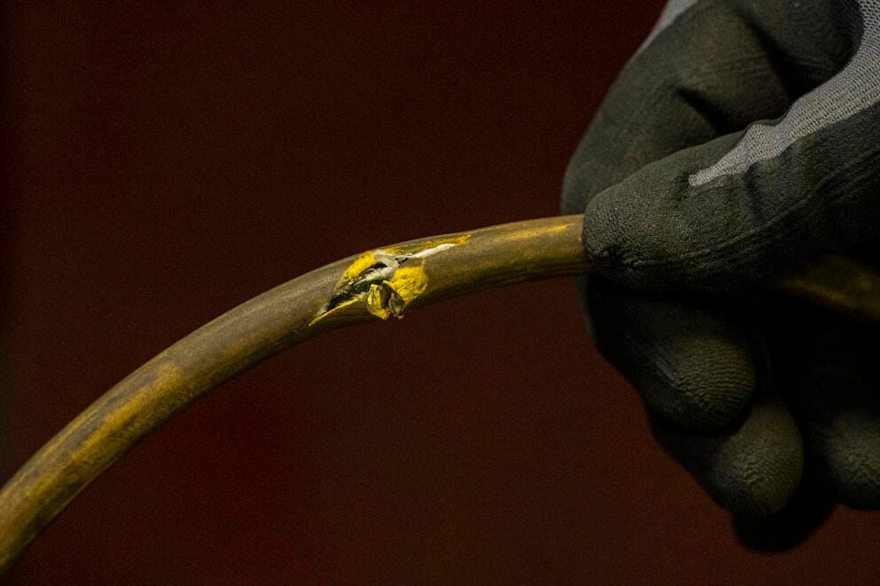 A close up of a gloved hand holding a frayed extension cord.