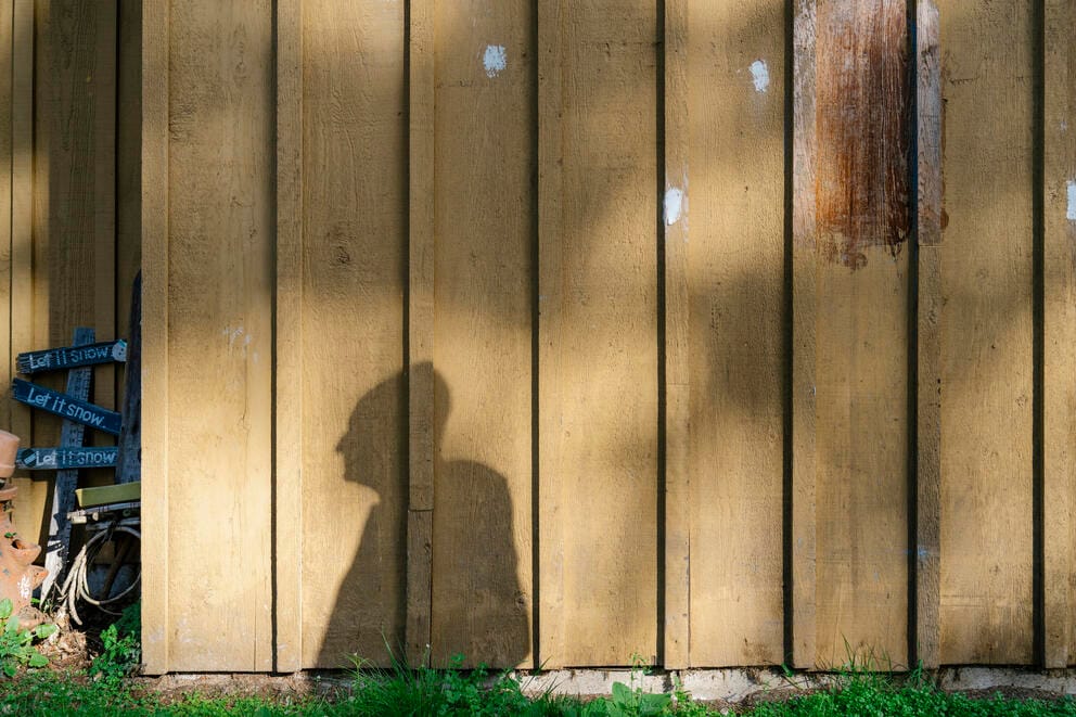 A shadow of a person is seen against a fence with lots of spackle on its boards.