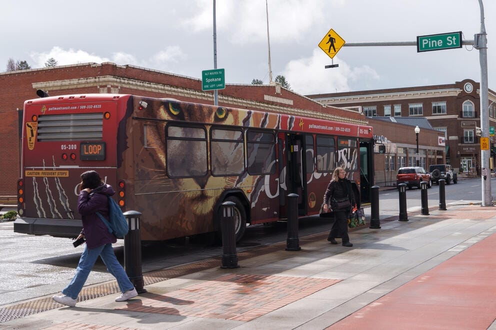 a bus advertising washington state university picks up riders on a sunny day