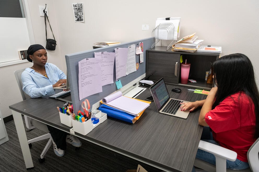 Two people work in a cubicle.