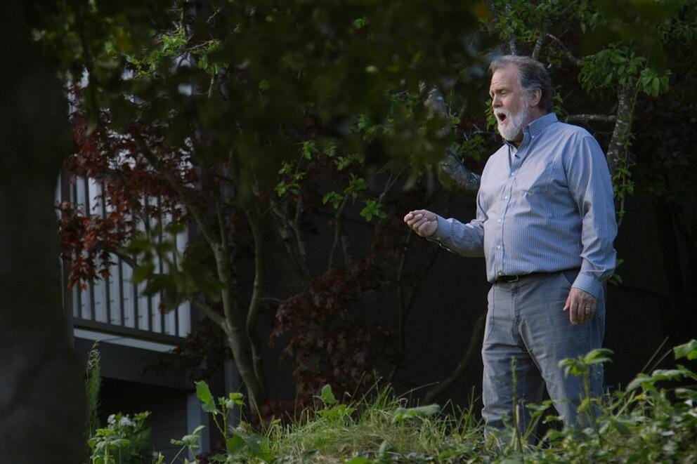 A film still of a man singing in the yard of a house