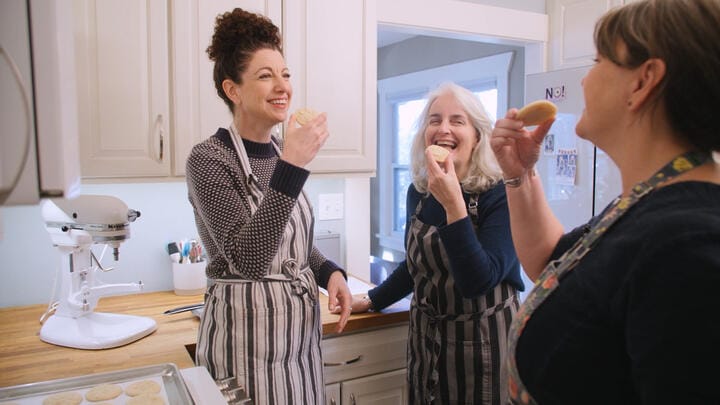 Three people eat cookies in a kitchen