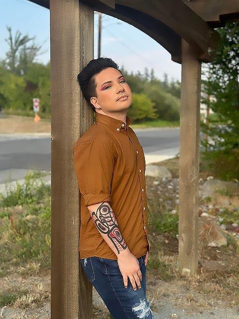 A person posing for a photo leans their back against a post.