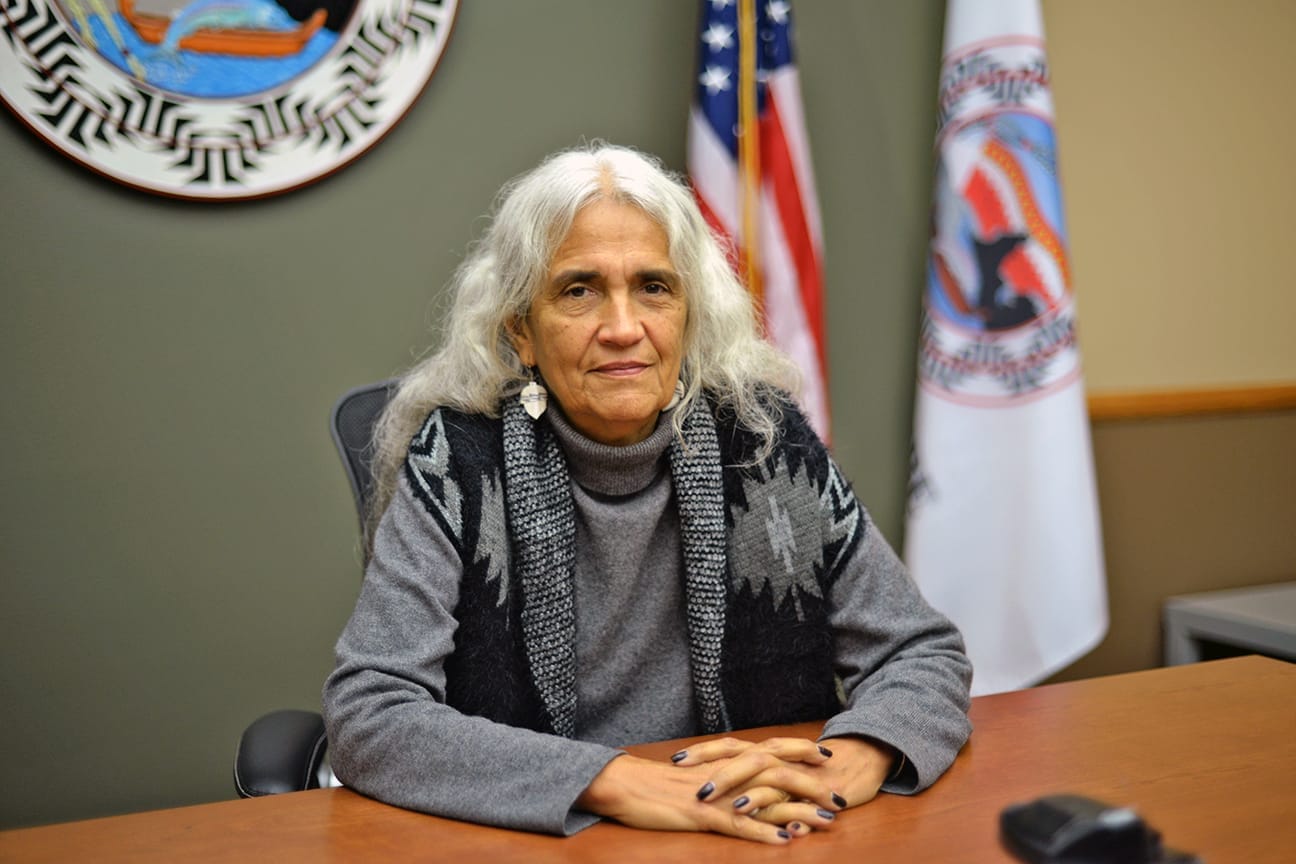 A casually dressed person poses for a photo behind a dais in a courtroom.