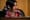a woman with black hair and a dark pink sweater speaks into a microphone at city hall