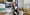 A girl with purple hair smiles while sitting in front of a computer with a notebook and pen.