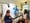 Two people sit talking in a kitchen with filming equipment set up