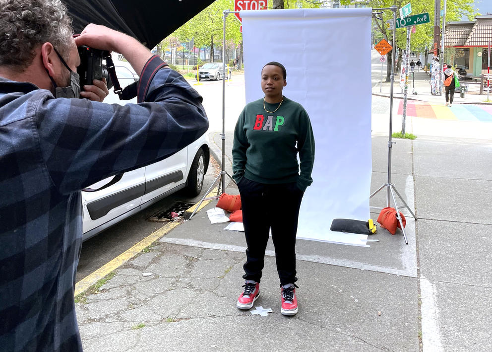 A photographer takes a picture of a person standing in front of a backdrop