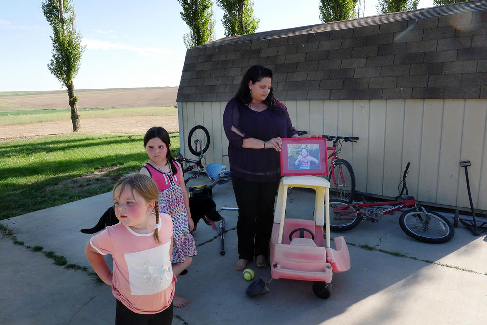 A woman stands outside with two young girls, balancing a picture frame on top of a child's car