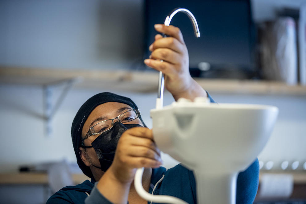 Sherae Lascelles looks closely at a part used to make a sink