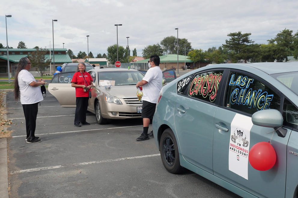 Three people stand outside a census 2020 decorated car