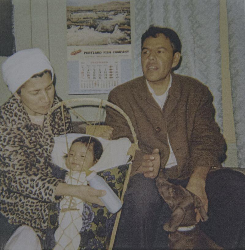 A woman tends to a baby in a bassinet while a man looks off camera and pets a dog